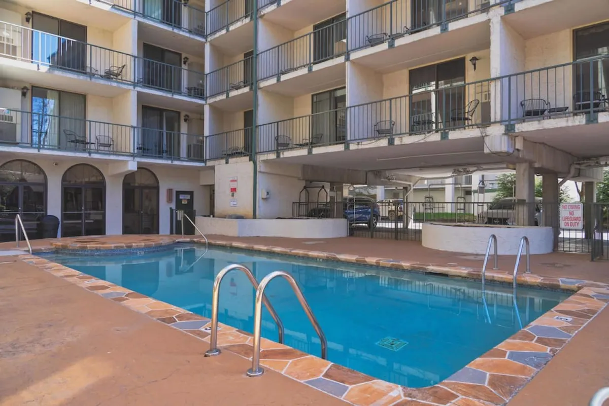 The image showcases the condo building’s inviting outdoor swimming pool, surrounded by sun loungers and balconies overlooking the water. The architecture is modern yet welcoming, and the scene suggests a relaxing atmosphere perfect for sunbathing, swimming, or socializing under the Tennessee sky.