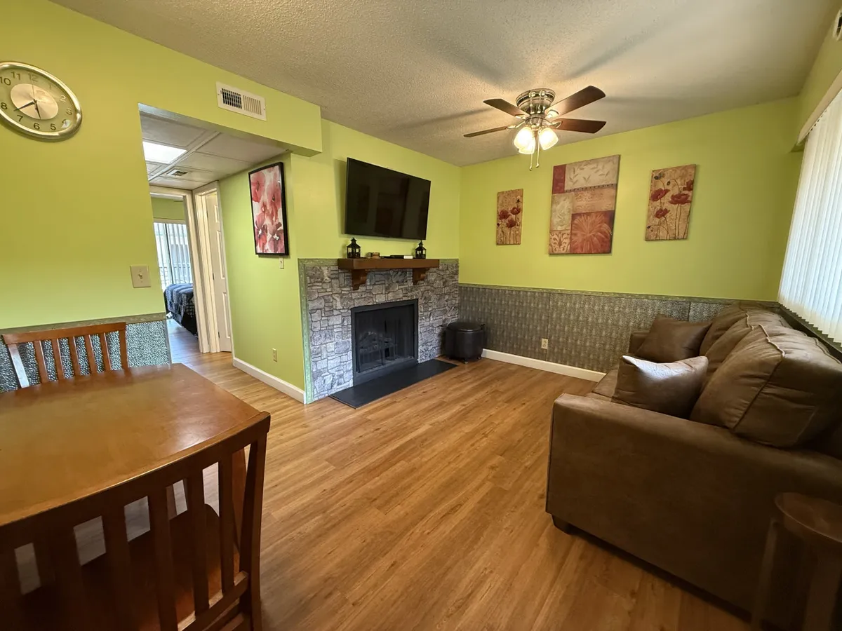 A cozy living area featuring a plush sofa, electric fireplace, dining table, television, and decorative wall art. The space exudes warmth and is designed for relaxation, entertainment, and family gatherings.