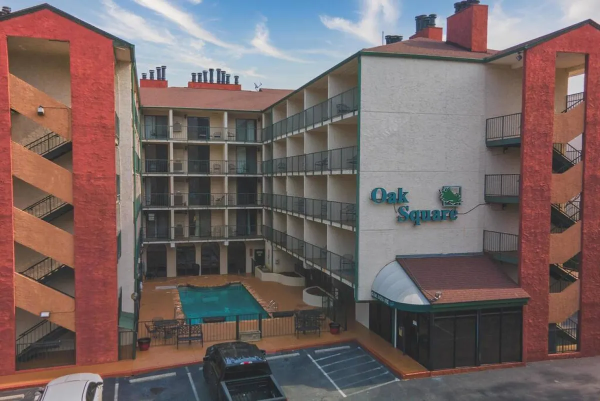 This image displays the Oak Square exterior, featuring the swimming pool, Oak Square sign, balconies, and a red brick facade. The pool area is active and inviting, suggesting a hub for families to unwind after a day of exploring nearby attractions.