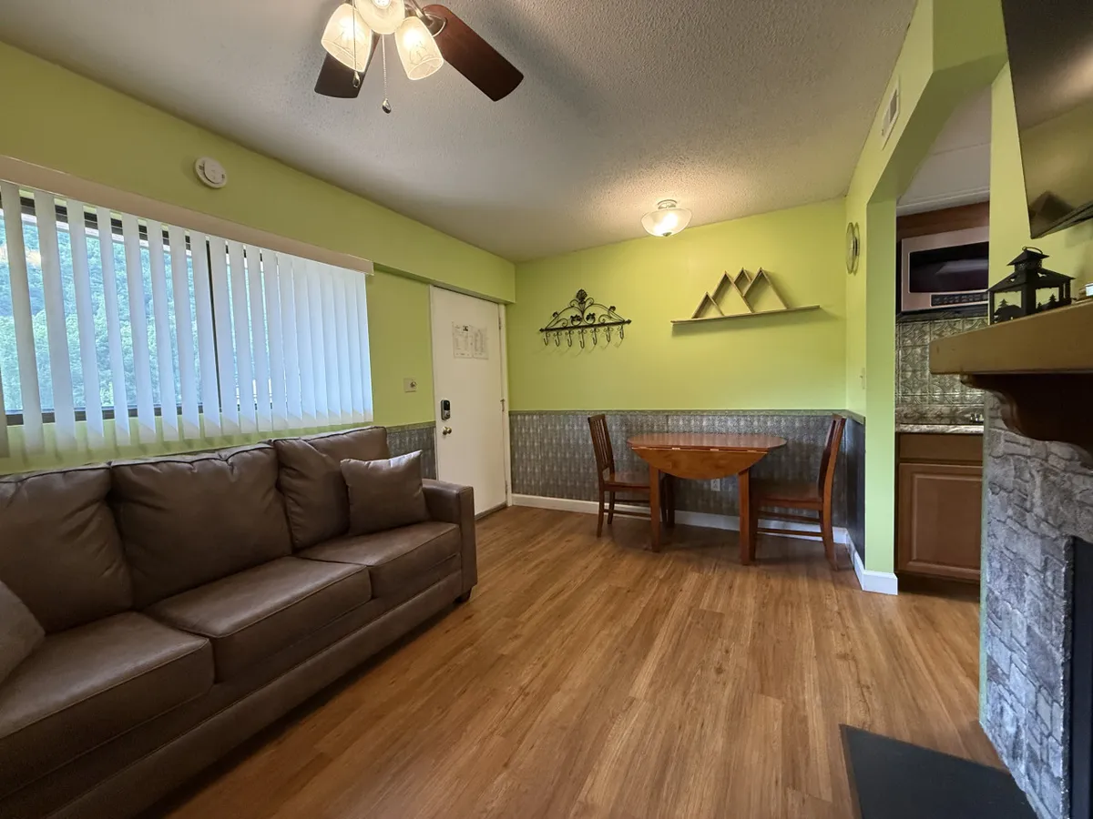 A warmly lit dining area with a wooden dining table and matching chairs, set adjacent to a cozy brown sofa. The inviting scene suggests a welcoming spot for shared meals, conversation, and laughter.