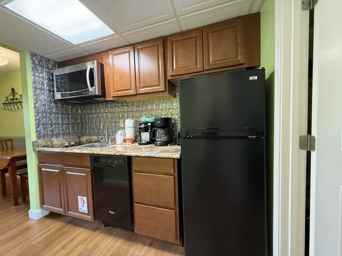 A cozy kitchenette area featuring cabinets, stainless steel appliances including a mid-size fridge, a countertop, and a kitchen sink. The scene conveys a practical and inviting space suitable for meal preparation and casual cooking.