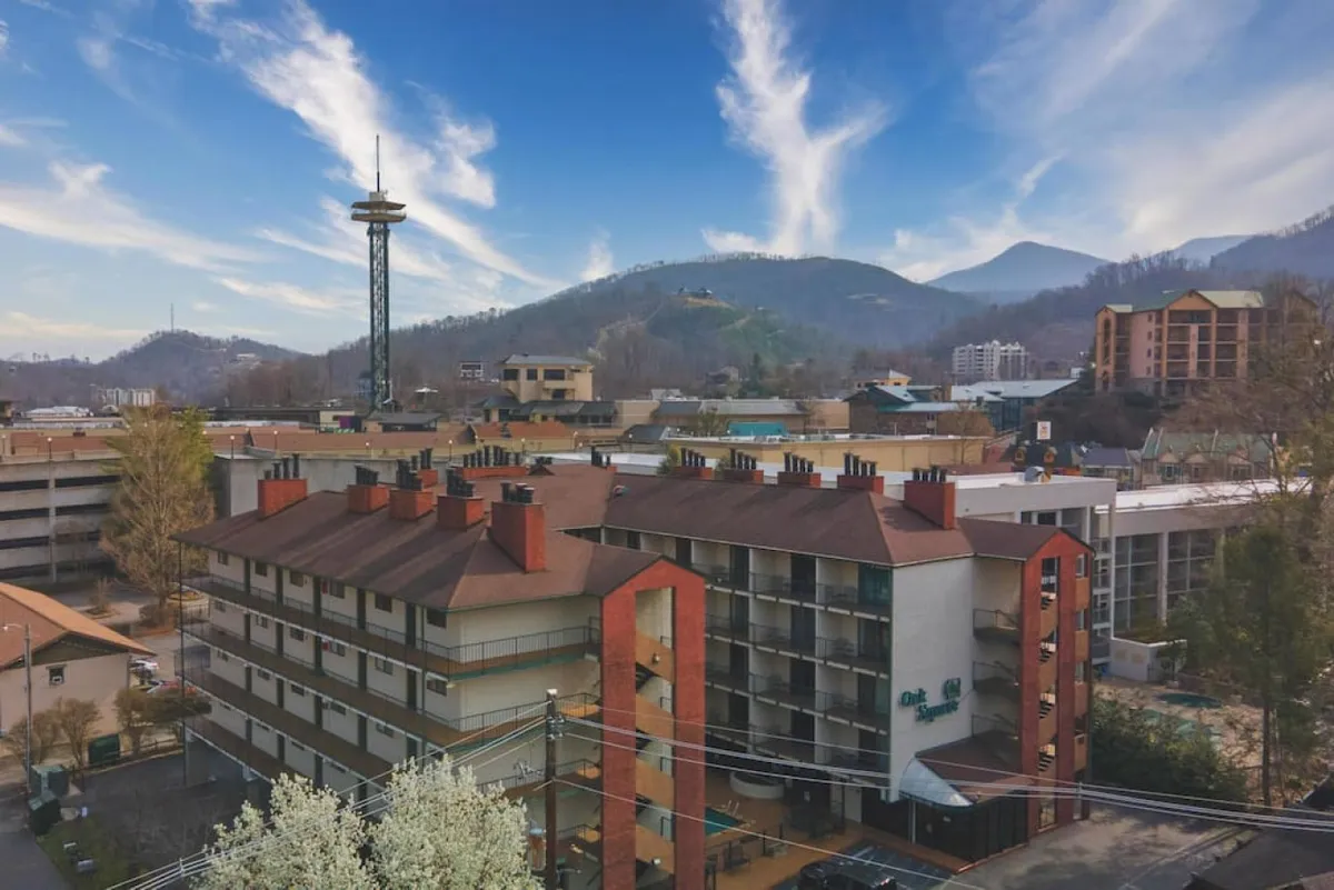 A wide-angle exterior view of the Oak Square hotel building set against scenic surrounding mountains with a communication tower in the background, communicating a sense of proximity to Gatlinburg’s attractions and the adventure opportunities of the area.