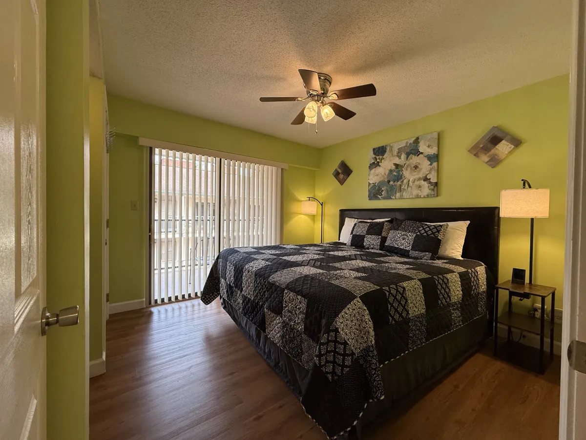 The image displays a serene bedroom featuring a plush king bed with a patterned quilt, decorative wall art, and large windows with blinds allowing natural light to filter in. The room exudes a calm and restful atmosphere, ideal for relaxation after a day of adventure.
