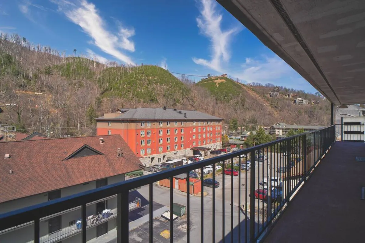 A scenic mountain view framed by a sturdy balcony railing, with a hint of the red building below. The vista is tranquil, offering guests a breathtaking natural backdrop to their stay.
